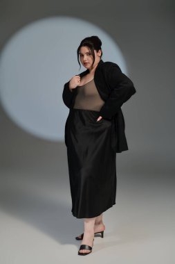 Güzel ve cüsseli bir kadın şık siyah elbiseler içinde zarif bir şekilde poz veriyor, eşsiz tarzını benimsiyor..