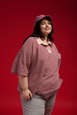 Şık ve cüsseli bir kadın dikkat çekici kırmızı bir ortamda gülümseyerek moda anlayışını sergiliyor..