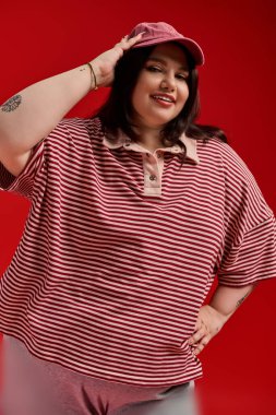 Çarpıcı, iri yarı bir kadın şık elbisesiyle canlı kırmızı bir arka plana karşı şık bir şekilde poz veriyor..