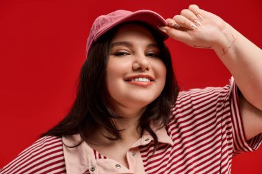 Kendine güvenen, kilolu, şık bir şapka takan ve gülümseyen bir kadının cesur moda ifadesi.