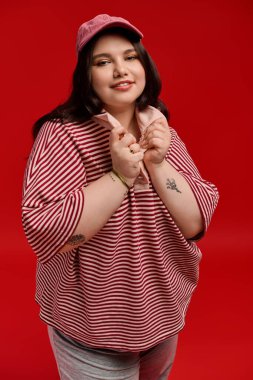 Şık bir kadın cazibesiyle poz veriyor, parlak kırmızı bir arka plana karşı elbisesini sergiliyor..