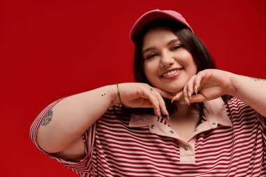 Çekici ve cüsseli bir kadın kırmızı arka planda sıcak bir tebessümle neşeli poz verir..