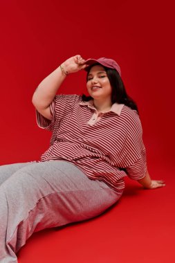 Güzel ve cüsseli kadın zarif bir şekilde kırmızı arka planda poz veriyor, şık kıyafetini sergiliyor..