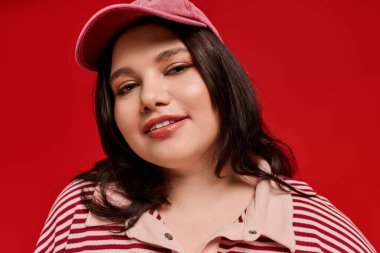 Güzel, iri cüsseli bir kadın şapkalı ve çizgili üst gülümsemeli moda anlayışını sergiliyor..