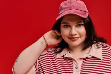 Artı cüsseli kadın canlı kırmızı arka planda şık kıyafetini gururla sergiliyor..