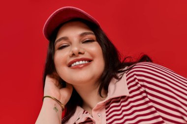 Güzel, iri cüsseli, şapkalı bir kadın neşeli bir şekilde poz veriyor, canlı stili ve çekiciliğiyle.