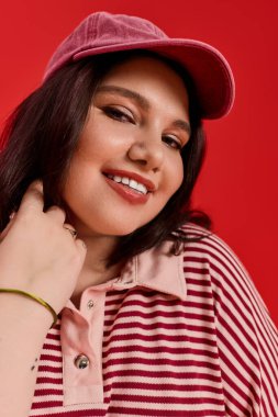 Neşeli, iri yarı bir kadın kendine has tarzını canlı kırmızı bir arka planda sergiliyor..