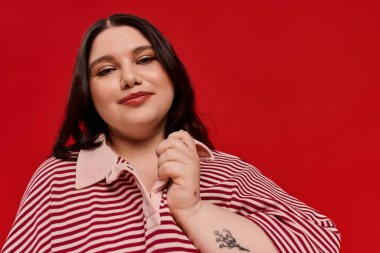 Bu şık kadın çizgili bir üst ve kalın kırmızı bir duvara karşı sıcak bir gülümseme içinde parlıyor..