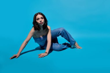 Şık genç bir kadın zarif bir şekilde parlak mavi bir arka planda poz veriyor, moda anlayışını ön plana çıkarıyor..