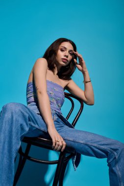 Modaya uygun genç bir kadın şık kıyafetlerini canlı renklerle sergileyerek zarif bir şekilde bir sandalyeye oturur..