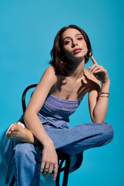 Çekici genç bir kadın şık kıyafetlerini ve kalın aksesuarlarını sergileyerek şık bir şekilde bir sandalyeye oturur..