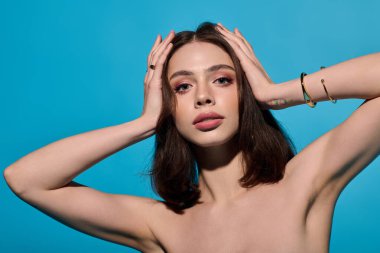 Güzel genç bir kadın kendine güvenerek poz veriyor çarpıcı mavi bir arka planla, tarzıyla hava atıyor..