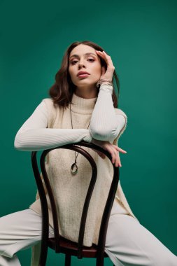 Sandalyedeki zarif kadın canlı yeşil bir arka plana karşı şık kıyafetini sergiliyor..