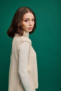 Genç bir kadın, canlı yeşil bir arka plana karşı şık giyinerek zarafet saçar..