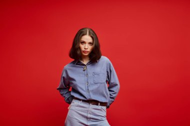 Güzel genç bir kadın bu çarpıcı kırmızı arka planda zerafetle moda tarzını sergiliyor..