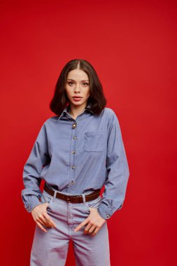 Genç bir kadın, modaya uygun tarzını kot gömlek ve pantolonuyla sergiliyor. Kendine güvenen bir poz veriyor..