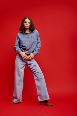 Kendine güvenen, modaya uygun giyinmiş genç bir kadın cesur bir kırmızı arka plana karşı çıkıyor..