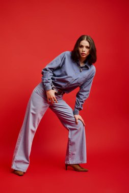 Şık genç bir kadın, canlı kırmızı bir arka plana karşı eşsiz bir kot giysisi modelliyor..