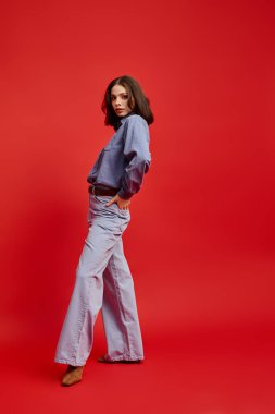 Genç, güzel bir kadın poz veriyor, kırmızı bir arka plana karşı kıyafetini sergiliyor..