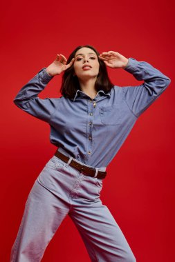 Kendine güveni olan şık genç bir kadın parlak kırmızı arka planda şık bir kot pantolon giyiyor..