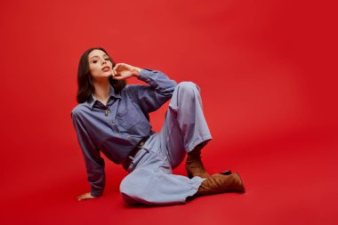 Genç, şık bir kadın zarif bir şekilde yerde otururken güzellik ve güven yayar..