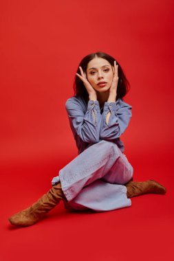 Modaya uygun genç bir kadın özgün tarzını sergileyen koyu kırmızı bir zemine karşı düşünceli bir şekilde poz veriyor..