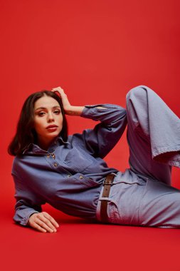 Genç kadın, parlak kırmızı bir yüzeyde uzanırken güzellik ve moda anlayışını sergiliyor..