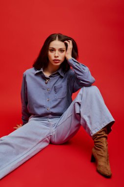 Kendine güveni tam genç bir kadın, kırmızı bir arka plana karşı şık bir elbiseyle poz veriyor..