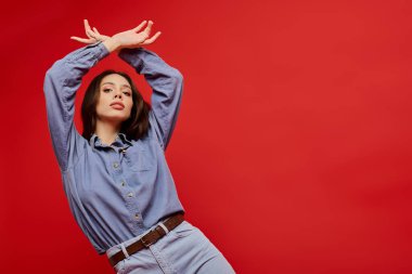 Modaya uygun genç bir kadın çarpıcı bir kırmızı arka planla kendine güvenen bir poz veriyor..