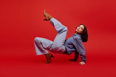 Tarz sahibi genç bir kadın dinamik bir poz veriyor, kırmızıya karşı modaya uygun kıyafetler giyiyor..