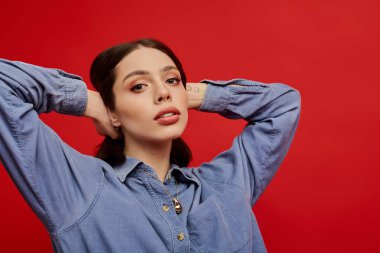 Şık bir kadın ellerini başının arkasına koyup moda kıyafetlerini ve makyajını sergiliyor..