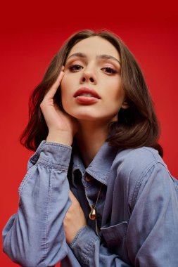 Zarif genç bir kadın çarpıcı bir kırmızı arka planda büyüleyici bir bakışla zarifçe poz verir..
