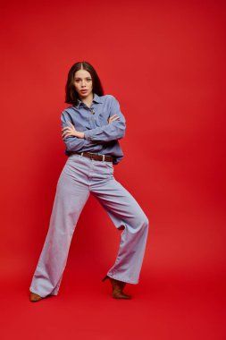 Genç ve güzel bir kadın, modaya uygun kot giyip, ışık saçan bir tarz ve cazibeyle poz veriyor..