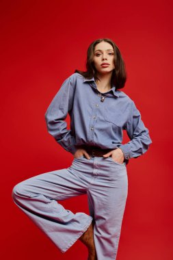 Güzel bir kadın şık kıyafetini gösterirken cesur bir kırmızı zemine karşı duruyor..