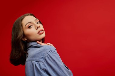 Şık bir kadın zarif bir şekilde kırmızı bir zemine karşı duruyor, moda anlayışını sergiliyor..