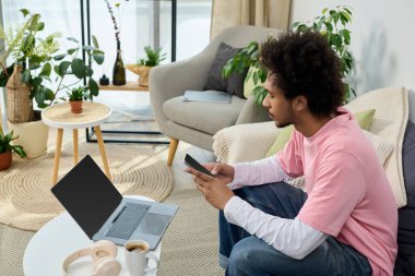 Pembe tişörtlü genç adam bir koltuğa oturur, telefonuna odaklanır..