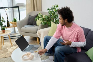 Genç adam bir içkiyle rahatlıyor, canlı, hoş geldin ortamında dizüstü bilgisayara odaklanıyor..