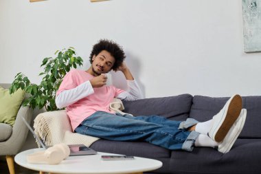 Genç yakışıklı adam kanepede dinleniyor, kahvesini yudumluyor ve şık bir evde dinleniyor..