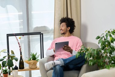 Genç bir adam yeşilliğin ortasında tabletini kullanarak şık bir sandalyede dinleniyor..