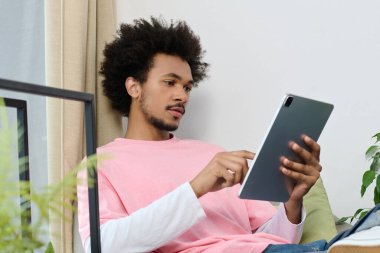 Rahat genç bir adam şık bir salonda tabletle etkileşime girer, huzurlu bir anın tadını çıkarır..