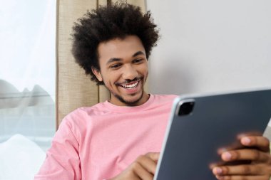 Gülümseyen genç bir adam tabletle etkileşime girer, neşeli ve rahat bir atmosfer yaratır..