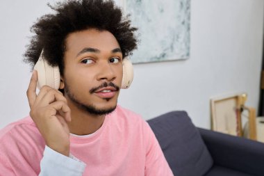 Modern bir mekanda kulaklık takmış genç bir adam müzik dinliyor, gülümsüyor..