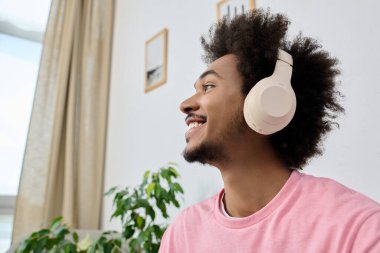 Parlak bir gülümseme kulaklığı olan genç bir adama, müziğe dalmış, çevresi yeşilliklerle çevrili..