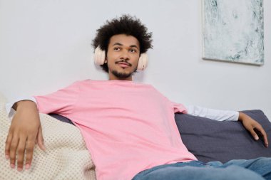 Kulaklıklı genç yakışıklı bir adam kanepede uzanıyor, müziğinin içinde kayboluyor..