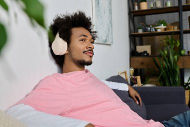 Neşeli genç adam müziğin keyfini çıkarırken şık bir yaşam alanında rahat bir kanepede dinleniyor.