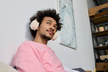 Genç yakışıklı bir adam, kulaklıklarıyla bir kanepede dinleniyor, müziğin rahatlatıcı seslerinde kayboluyor..