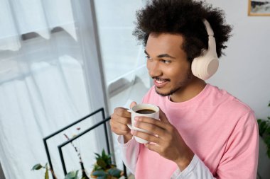 Genç yakışıklı bir adam kulaklık takarak kahvesini yudumluyor, evinde dinlendirici bir ana dalmış..