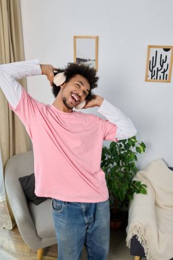 Kulaklıklı rahat bir genç adam şık bir oturma odasında dans ederken geniş bir gülümseme sergiliyor..