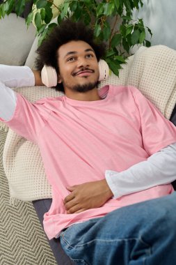 Neşeli bir suratı olan genç bir adam kanepeye uzanıp kulaklıkla müzik dinliyor..