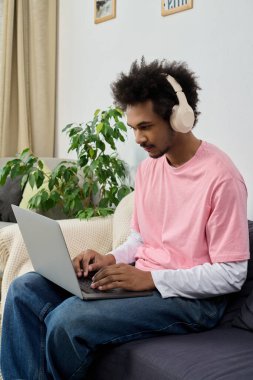 Kulaklık takan genç yakışıklı bir adam evinde rahatça otururken dizüstü bilgisayarına odaklanıyor..